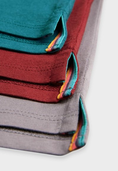 Gomila štirih teksturiranih tkaninskih servietov: teal, burgundska, siva. Vsak ima kontrastno obrobo in detajl z zanko v živahnih črtah.