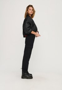 Zwarte gewatteerde bomberjack met een cropped fit en elastische zoom, gecombineerd met hoge cargobroeken en zwarte veterschoenen.