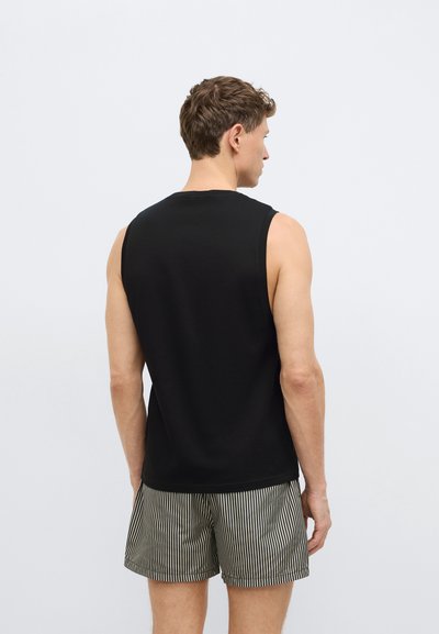 Μαύρο αμάνικο μπλουζάκι με στρογγυλή λαιμόκοψη, φορεμένο πάνω από ριγέ σορτς. Το μπλουζάκι έχει ομαλή υφή και εφαρμοστή σχεδίαση.