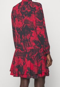 Rood bloemenpatroon jurk met lange mouwen en een gelaagde rok. De stof heeft een zachte textuur en het ontwerp heeft donkere accenten.