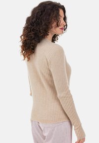 Beiger, gerippter Pullover aus weichem Stoff mit langen Ärmeln und tailliertem Schnitt sowie leicht geschwungenem Saum.