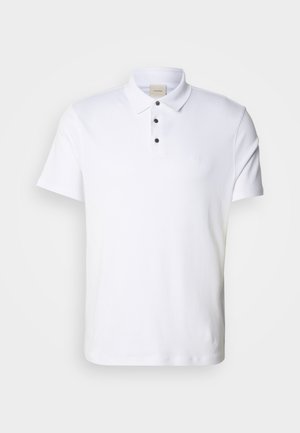 Polo blanco hecho de algodón, con cuello, tapeta de tres botones con botones negros y un sutil detalle de logo en el pecho.