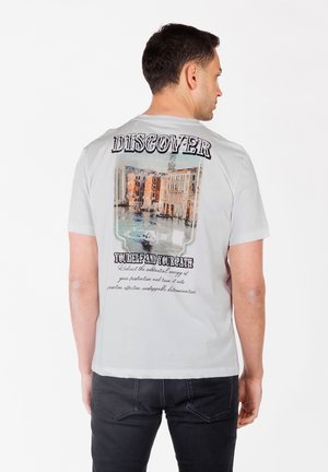 Camiseta gris claro con un gráfico colorido de una escena veneciana en la parte trasera, con texto negro en negrita arriba y abajo de la imagen.