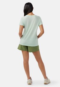 Camiseta atlética de manga corta en verde claro con cuello redondo, combinada con pantalones cortos en verde olivo. La tela parece ligera y transpirable.