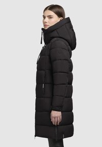 Abrigo acolchado negro con una capucha amplia, diseño acolchado, forma ajustada, bolsillos con cremallera y detalle de logo en la manga. Textura suave.