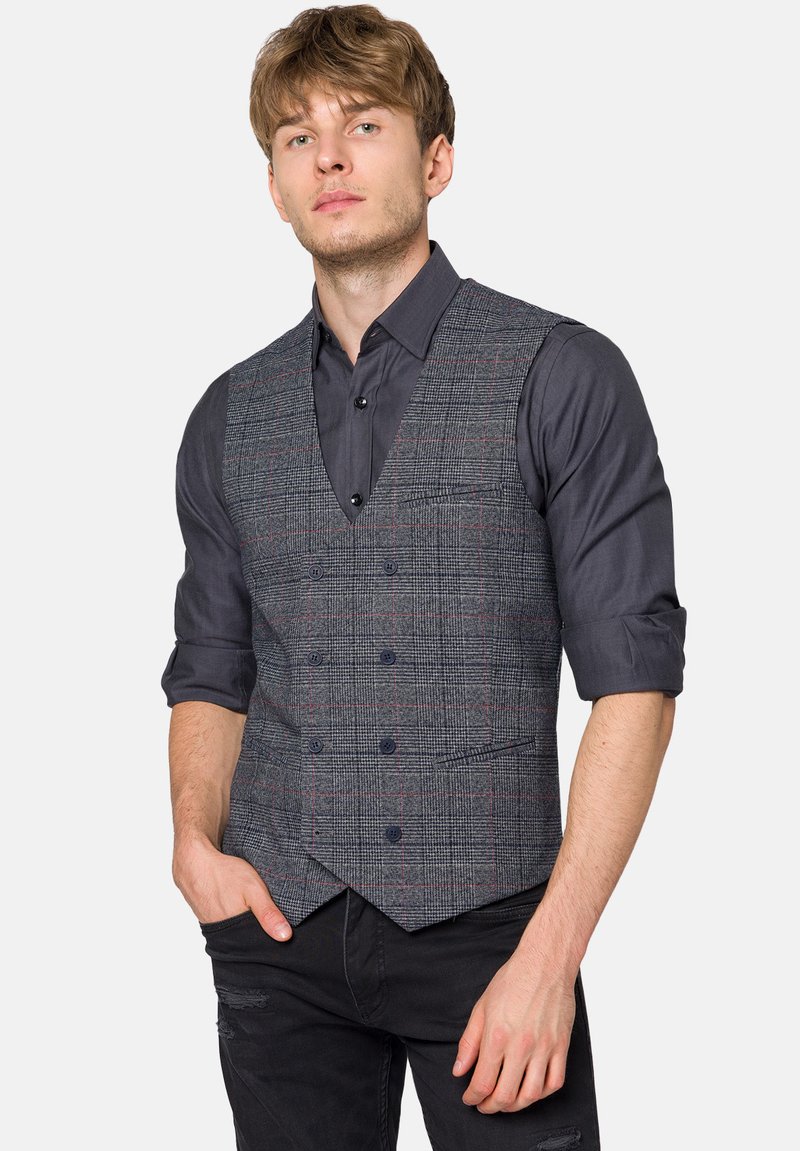 Szary kamizelka w kratę z czerwonymi akcentami, z dekoltem w serek i pięcioma guzikami, noszona na ciemnej koszuli; stylizowana z czarnymi dżinsami.