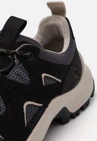 Sapatilha preta e cinza com materiais em malha e camurça, colarinho acolchoado, língua texturizada e sola de borracha com ranhuras profundas.