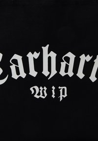 Tissu noir avec une lettrage gothique audacieux en blanc. Le texte comprend "Carhartt" et "wip", avec des détails décoratifs et des bords tranchants.