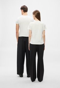 Λευκές βαμβακερές μπλούζες με κοντά μανίκια, σε συνδυασμό με μαύρο, ψηλόμεσο και φαρδύ παντελόνι. Μινιμαλιστικός σχεδιασμός χωρίς ορατά σχέδια ή διακοσμητικά στοιχεία.