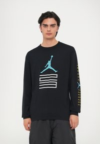 Must muströps T-särk, millel on sinine Jordan logo ja valge graafiline kujundus ees, ning kollane tekst varrukal.