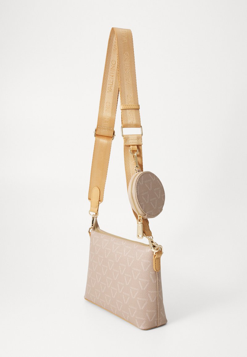Sac bandoulière en tissu beige avec motif logo géométrique, bandoulière réglable beige clair, quincaillerie dorée, et pochette ronde détachable.