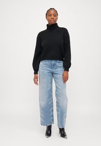 Maglione a collo alto lavorato a maglia nera, vestibilità rilassata. Jeans larghi blu chiaro con dettagli strappati. Stivali alla caviglia neri con tacco alto.