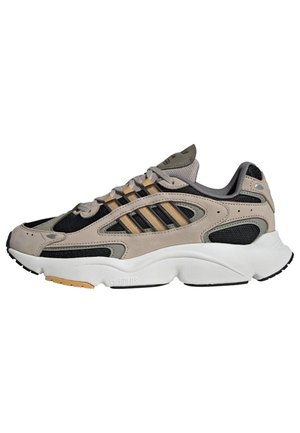 Beige og sort atletiksneaker med meshpaneler, beige striber, polstret hvid sål og snørelukning.