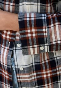 Geruite shirt met een mix van marineblauw, wit en roestkleur. Zacht, lichtgewicht materiaal met knoopsluiting en contrasterende manchetten.