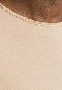 Light peach shirt featuring a scoop neckline, soft texture, and a slightly frayed edge, with a smooth, simple design and no patterns.