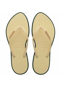 Infradito in gomma beige con soletta testurizzata, suola verde e sottili cinghie; presenta il nome del marchio su una cinghia.