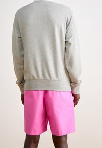 Szara bawełniana bluza dresowa z prążkowanymi mankietami i dolnym ściągaczem, zestawiona z jasnoróżowymi szortami. Widoczne przeszycia i elastyczny pas w talii.