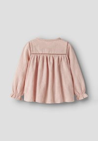 Blusa per bebé a maniche lunghe di un delicato colore rosa chiaro, con pizzo sul corpetto, schiena arricciata e polsini con volant su uno sfondo grigio.