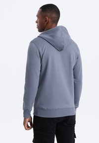 Sweat à capuche de couleur grise, avec une texture douce, des poignets et un ourlet côtelés, et une coupe décontractée, avec une capuche bien visible.