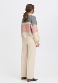 Maglione oversize a maglia con strisce grigie, rosa e beige, dal taglio rilassato. Abbinato a pantaloni beige a vita alta e scarpe basse scure.