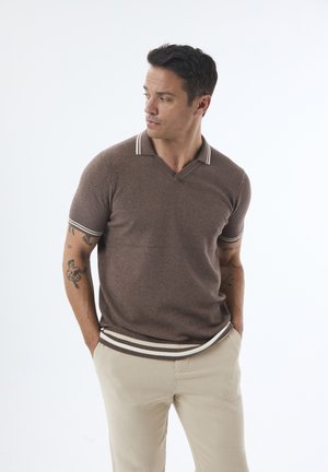 Polo de color marrón con textura y sutiles rayas blancas en el cuello y las mangas, combinado con pantalones beiges. Diseño sencillo y ajustado.