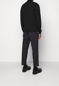 Maglione nero a dolcevita, slim fit, abbinato a pantaloni grigi scuri a gamba affusolata. Scarpe nere stringate con suola spessa. Nessun motivo visibile.