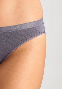 Graue Bikini-Hose mit Punkten und einem glatten Bund, der ein Logo trägt, aus weichem Material gefertigt und mit einem tiefen Schnitt gestaltet.