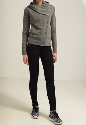 Szara bluza z kapturem na zamek błyskawiczny i asymetrycznym kołnierzem, w zestawieniu z czarnymi slim-fit jeansami i wzorzystymi czarnymi trampkami. Gładka faktura, nowoczesny design.