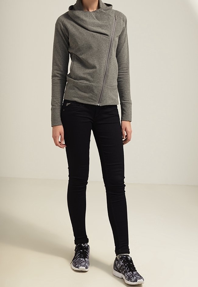 Šedá mikina na zip s asymetrickým límcem, spárovaná s černými úzkými džíny a vzorovanými černými teniskami. Hladká textura, moderní design.