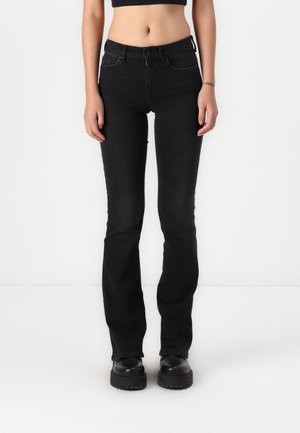 Kobieta nosząca czarne slim-fit jeansy z wysokim stanem oraz czarne buty na platformie stoi na białym tle.