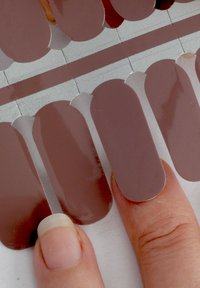 Nagelstickmuster in verschiedenen Beigetönen mit glänzender Oberfläche. Eine Probe wird zur Vergleichbarkeit gegen eine Fingerspitze gehalten.