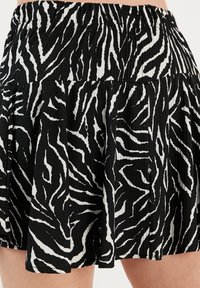 Črno-bele zebra črte nabrane krilo z elastičnim pasom, ki se ponaša z gladko teksturo in plastično zasnovo.