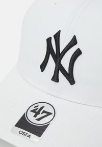 Cappello da baseball bianco con un prominente logo 'NY' ricamato in nero. Presenta una superficie liscia e un'etichetta circolare nera e argento con la scritta '47 OSFA.'