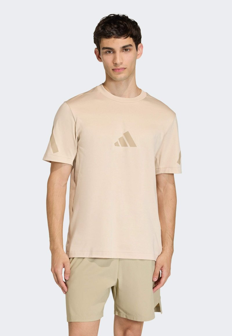 Camiseta beige de manga corta hecha de tela ligera, con un logo central, combinada con pantalones cortos beige a juego, que llegan por encima de la rodilla.