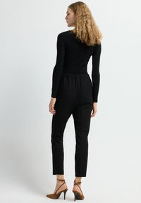 Zwarte geribbelde langemouwen top in combinatie met op maat gemaakte zwarte broeken met een elastische tailleband. Draag het met tan gekleurde hak sandalen.