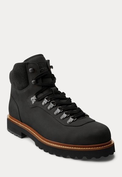 Zwarte leren wandelschoen met gewatteerde enkel, dikke zwarte veters, metalen oogjes, bruine rand en robuuste zwarte zool.