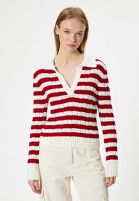 Rood-witte gestreepte gebreide trui met een diepe V-hals en geribbelde manchetten. Heeft een textuurdesign en een grote, zachte kraag.