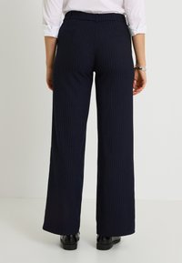 Pantalones de pierna ancha a rayas marineras con un ajuste entallado, que presentan una textura suave y una cinturilla de altura media. Se llevan zapatos negros.