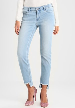 Lyseblå slim-fit jeans med frynser i kanterne og slidser foran, båret med en hvid sweater og lyserøde glitrende højhælede sko.