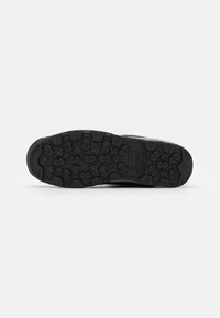 Suela de zapato atlético negro con un patrón texturizado para el agarre; material de goma; presenta ranuras y formas elevadas para la tracción.