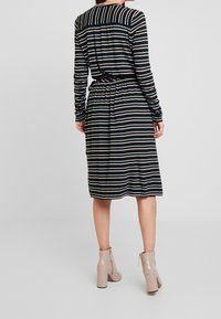 Zwart en beige gestreepte jurk tot halverwege met lange mouwen, gathered taille en achterkant met strikdetail; gecombineerd met naakte enkellaarsjes met hak.