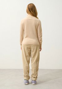 Beige Rollkragenpullover aus Strick, kombiniert mit hellbeigen Cordhosen. Die Hosen haben ein texturiertes Muster und hochgekrempelte Säume.