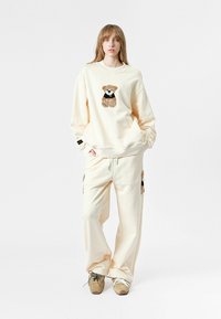 Sudadera extragrande de crema con bordado de oso, combinada con joggers a juego que presentan detalles de oso. Mezcla de algodón, corte relajado, puños acanalados.