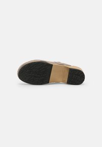 Semelle d'une chaussure beige avec des grips en caoutchouc noirs texturés au talon et à l'orteil, avec une section lisse fauve au milieu.