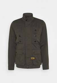 Oliwkowa kurtka wykonana z wytrzymałego materiału, z wysokim kołnierzem, czterema przednimi kieszeniami, czarnymi guzikami i markową żółtą metką.