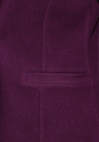 Lila stickad plagg med en slät textur, featuring en sidficka och strukturerade sömmar, som visar upp en skräddarsydd silhuett.