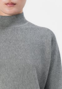 Close-up of a person wearing a gray ribbed turtleneck sweater, showing the neck and upper torso against a white background.