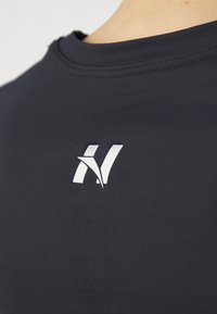 Crna majica kratkih rukava s okruglim izrezom, s bijelim logotipom na prsima. Materijal izgleda gladak i prilagođen tijelu.