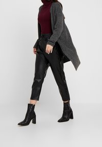 Donkergrijze cardigan, getailleerde bordeauxrode coltrui, zwarte nep leren cropped broek en zwarte enkellaarsjes met een blokhak. Gladde texturen en strakke lijnen.