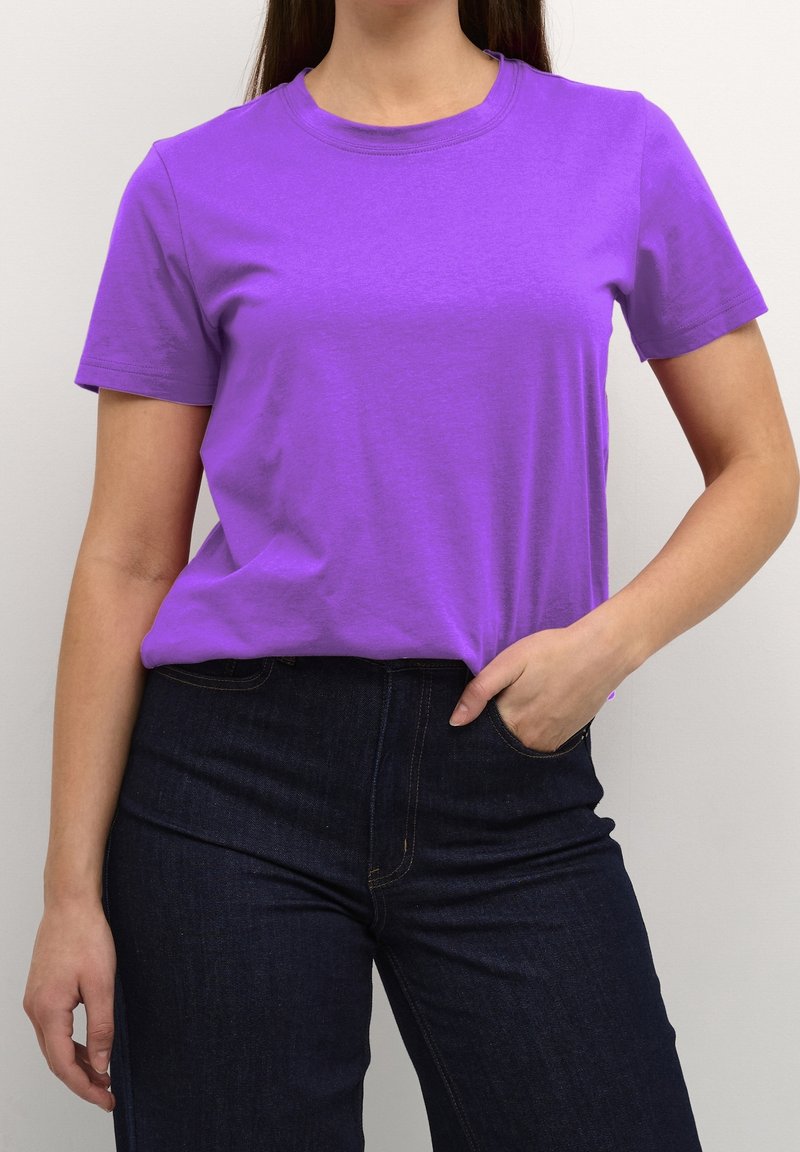 T-shirt en coton violet avec un col rond et des manches courtes, associé à un jean en denim foncé, présentant une coupe ajustée et une texture lisse.